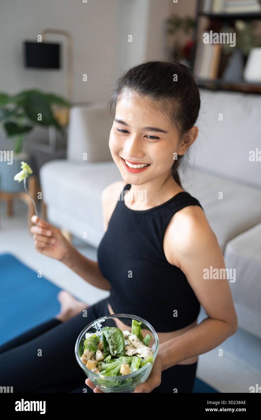 Fitness donna asiatica che mangia insalata sana dopo l'allenamento. Sorridendo bella ragazza asiatica che mangia cibo sano dopo l'esercizio Foto Stock
