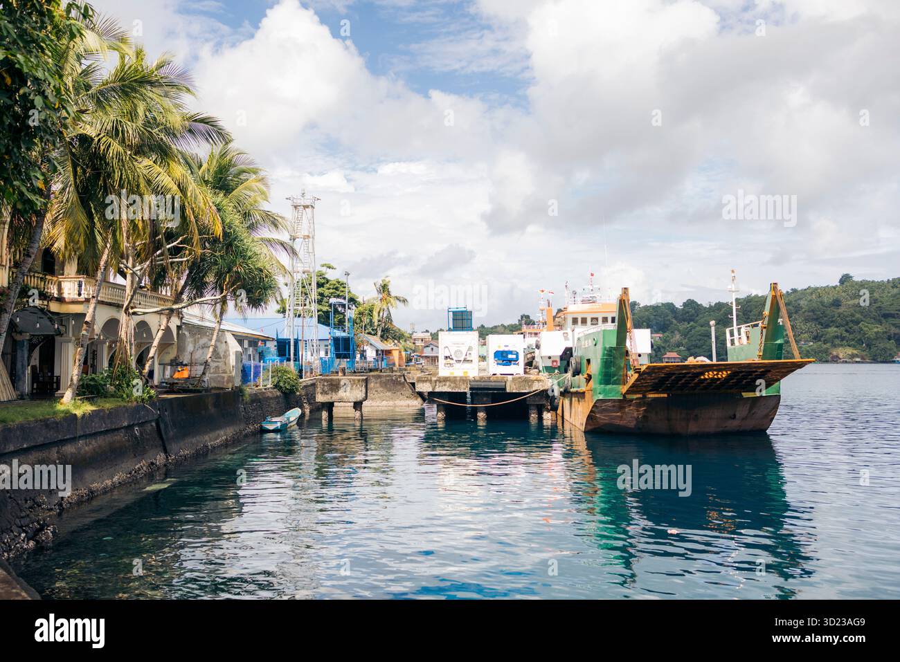 Un tranquillo porto con navi ormeggiate, alberi lussureggianti e cieli nuvolosi sull'acqua calma. Banda Neira, banda, Maluku centrale, Indonesia Foto Stock