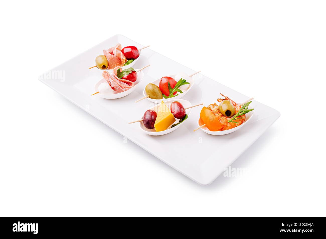 Le tapas assortite disposte ordinatamente su un piatto bianco includono carni, olive e frutta. Ideali per le riunioni, questi piccoli morsi sono colorati e pronti per l'uso Foto Stock