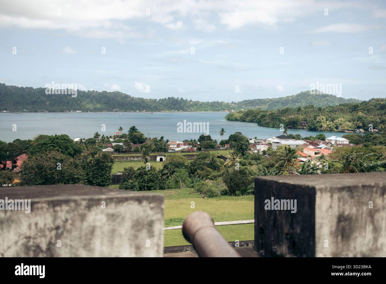 Una vista panoramica su un lussureggiante paesaggio verde con un lago e colline lontane sotto un cielo parzialmente nuvoloso. Banda Neira, banda, Reggenza centrale di Maluku, Indonesia Foto Stock
