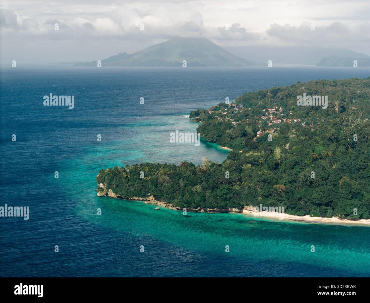 Vista aerea di una lussureggiante costa verde con acque cristalline e un'isola lontana. Pulau ai o ai Island, banda, Central Maluku Regency, Maluku, Indonesia Foto Stock