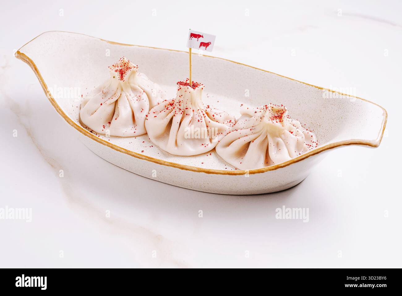 Tre gnocchi di manzo georgiano di khinkali presentati in un piatto di ceramica, conditi con scaglie di pepe rosso finemente macinati e una piccola bandiera Foto Stock