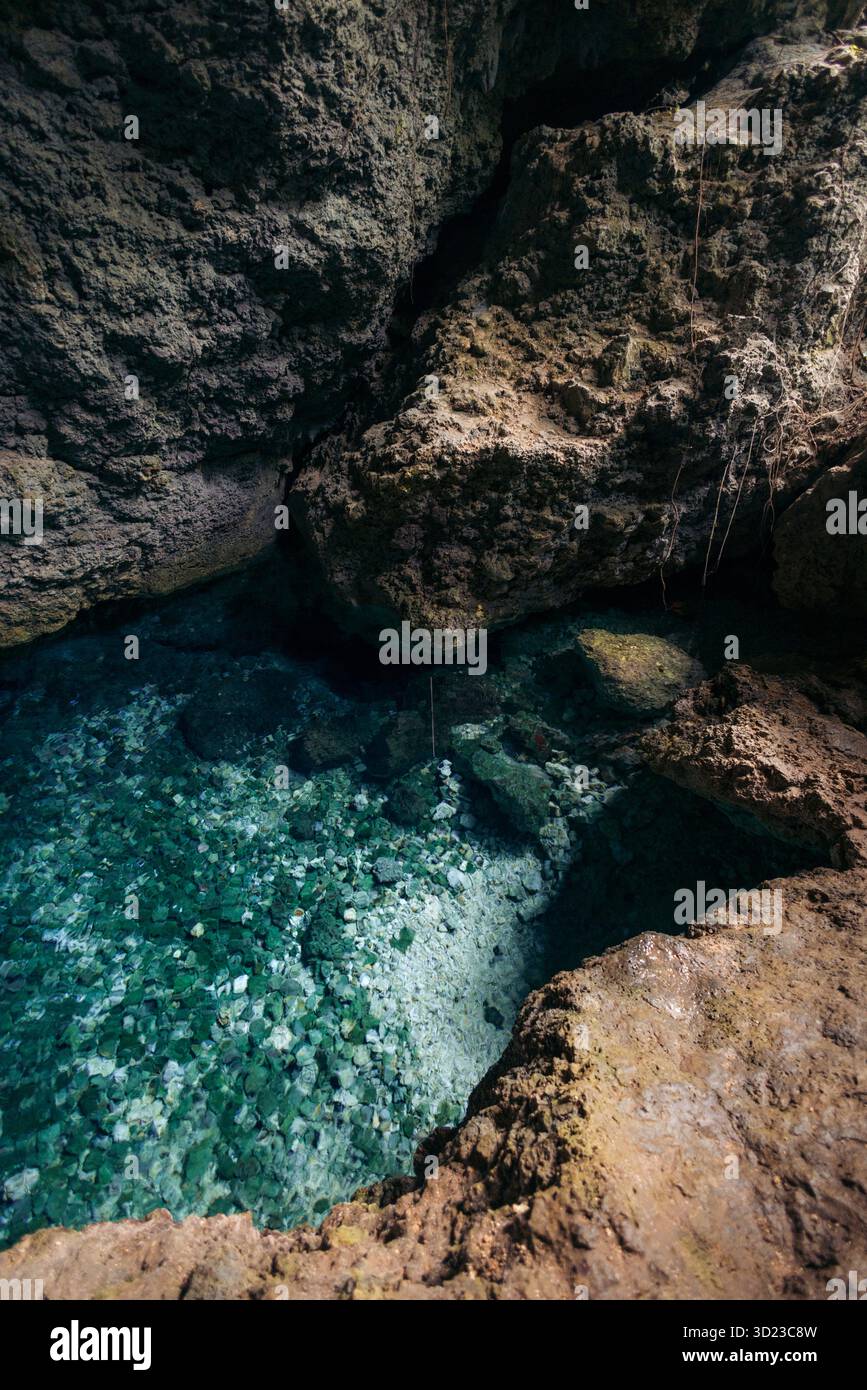 Piscina di acque turchesi cristalline circondata da formazioni rocciose ruvide e strutturate in un ambiente di grotta. Air Goa Hawang o Hawang Water Cave a Kei Kecil, Maluku sud-orientale, Indonesia Foto Stock