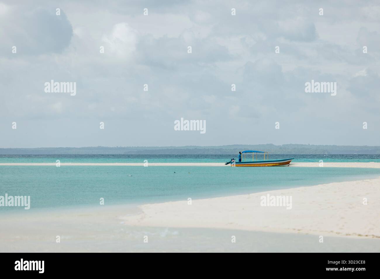Una piccola barca con un baldacchino galleggia su acque turchesi vicino a una spiaggia sabbiosa sotto un cielo nuvoloso. Pantai Ngurbloat o Ngurbloat Beach a Kei Kecil, sud-est di Maluku, Indonesia Foto Stock