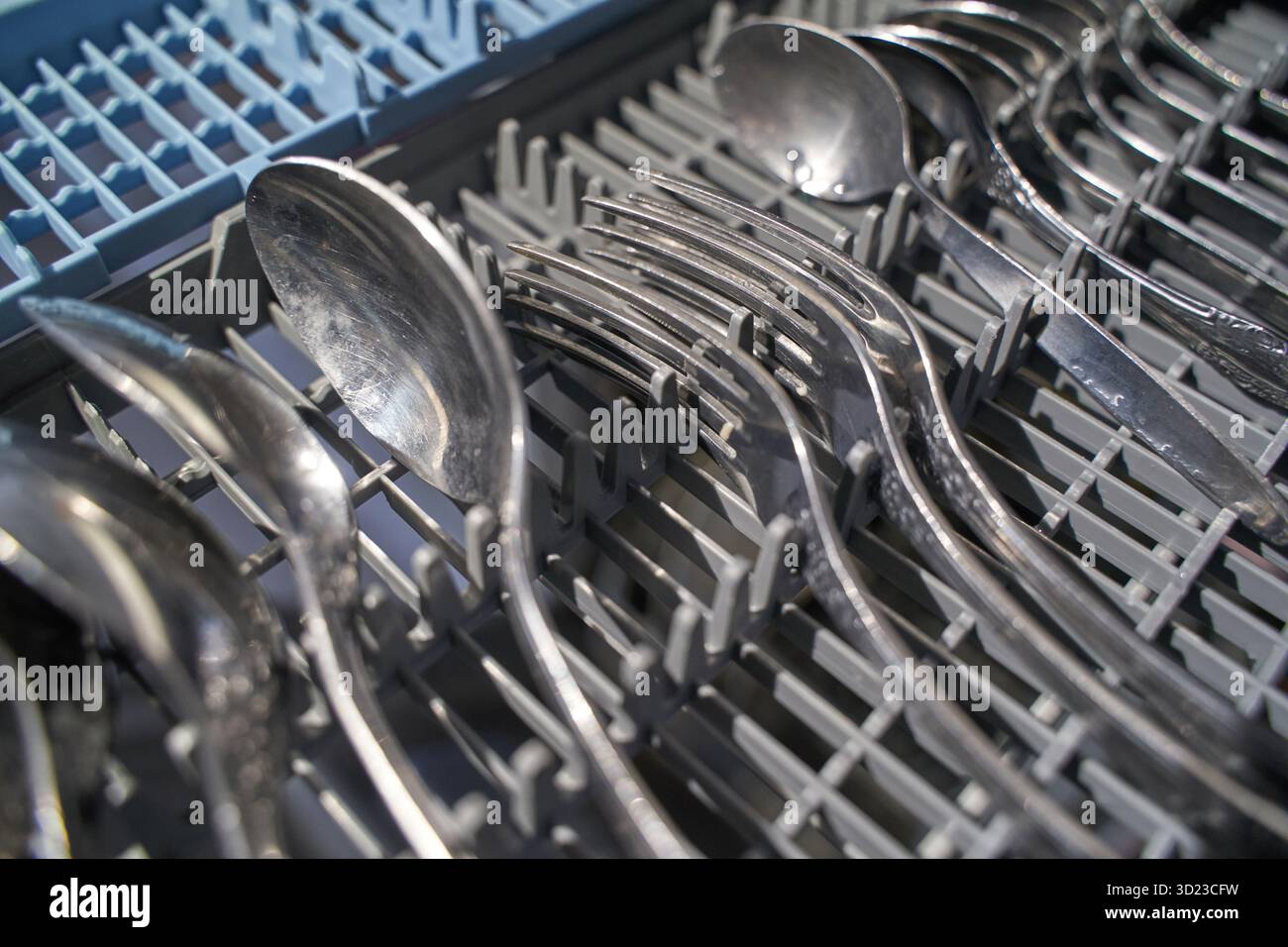 Primo piano di argenteria pulita nella griglia della lavastoviglie concentrata sugli utensili Foto Stock