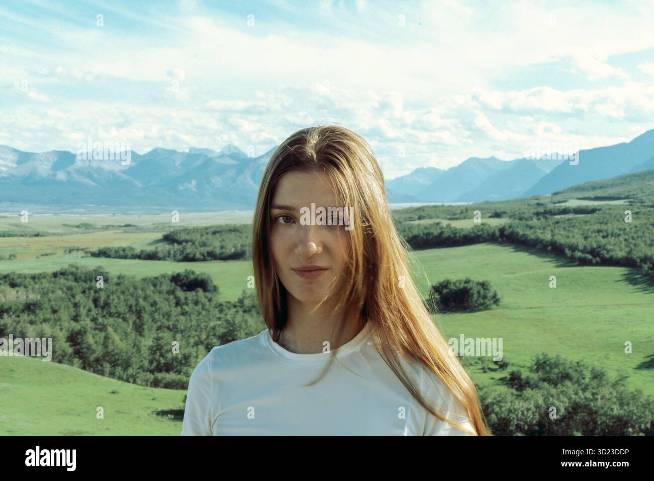 Giovane donna in un paesaggio naturale, con montagne e campi verdi intorno. Pincher Creek, Alberta Foto Stock