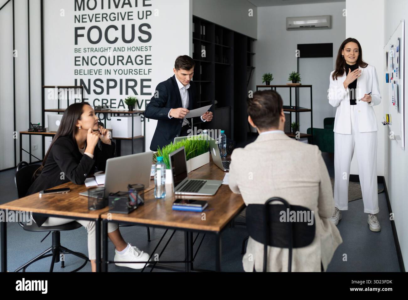 Donna che presenta un rapporto sul brainstorming del tempo in un ufficio elegante di fronte a diversi dipendenti nazionali Foto Stock