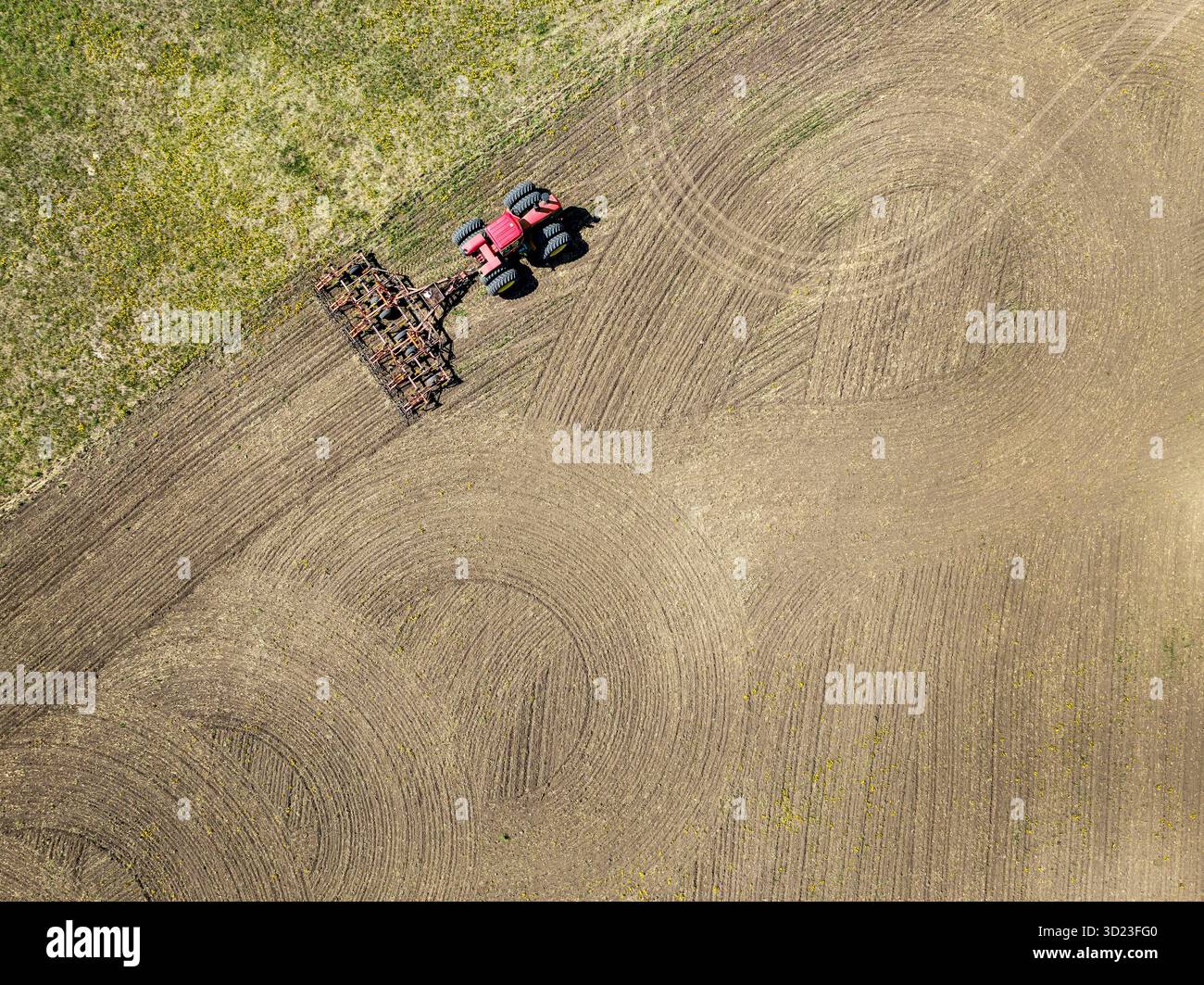 Vista aerea di un trattore rosso che ara un vasto campo con schemi intricati nel terreno. A nord di Calgary, Canada Foto Stock