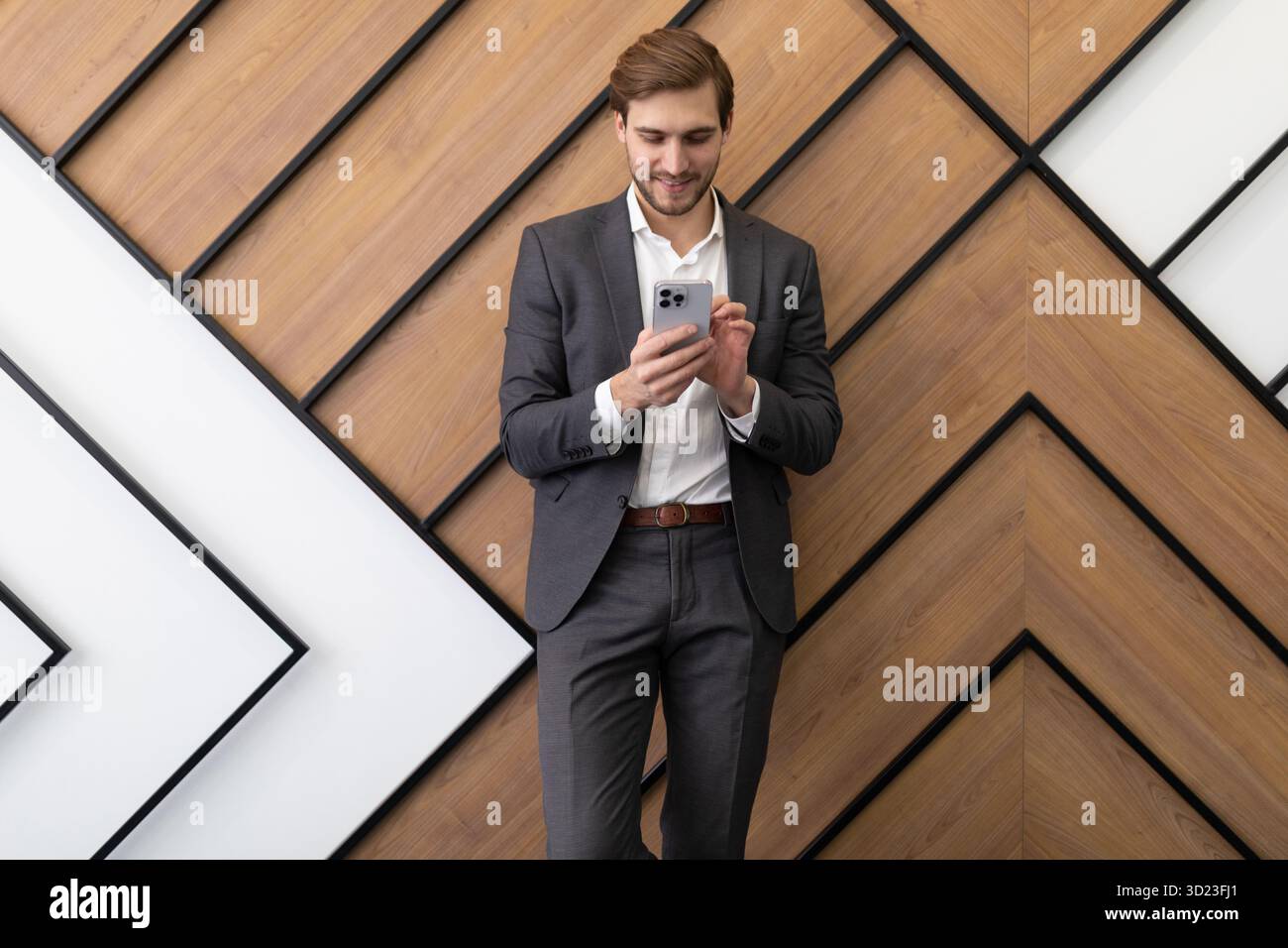 Un uomo d'affari sta scrivendo un messaggio in uno smartphone mentre è in ufficio Foto Stock