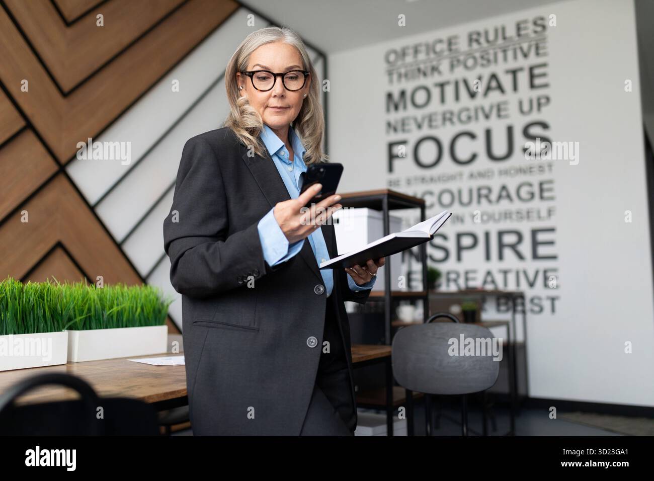 Donna d'affari anziana di mezza età in ufficio con un telefono in mano Foto Stock