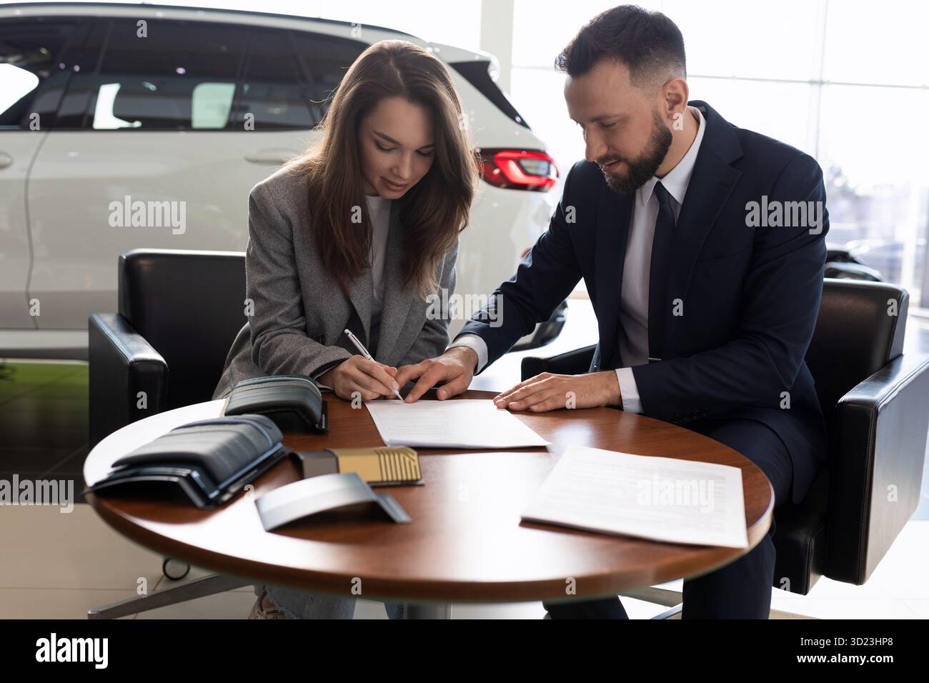 Una giovane donna e un manager delle vendite di auto firmano un contratto Foto Stock