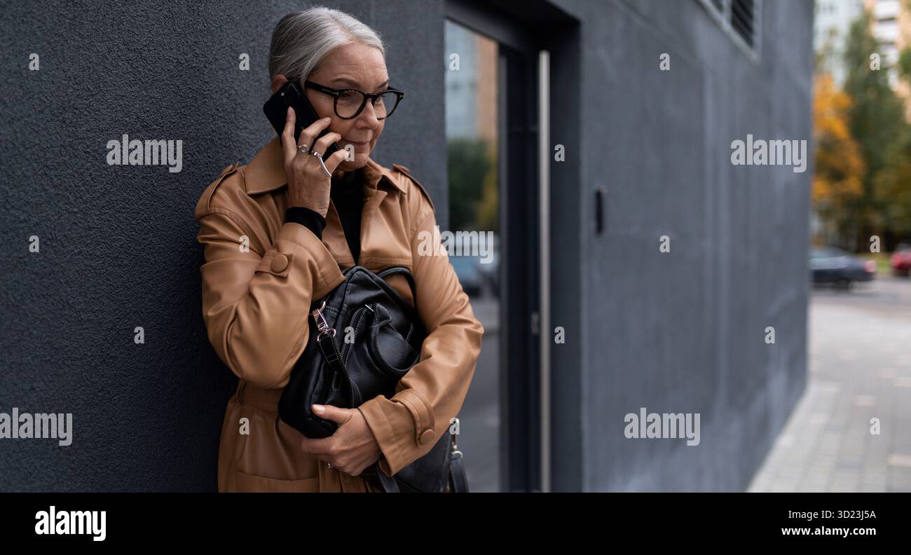 Donna anziana che parla su un telefono cellulare all'ingresso dell'ufficio Foto Stock