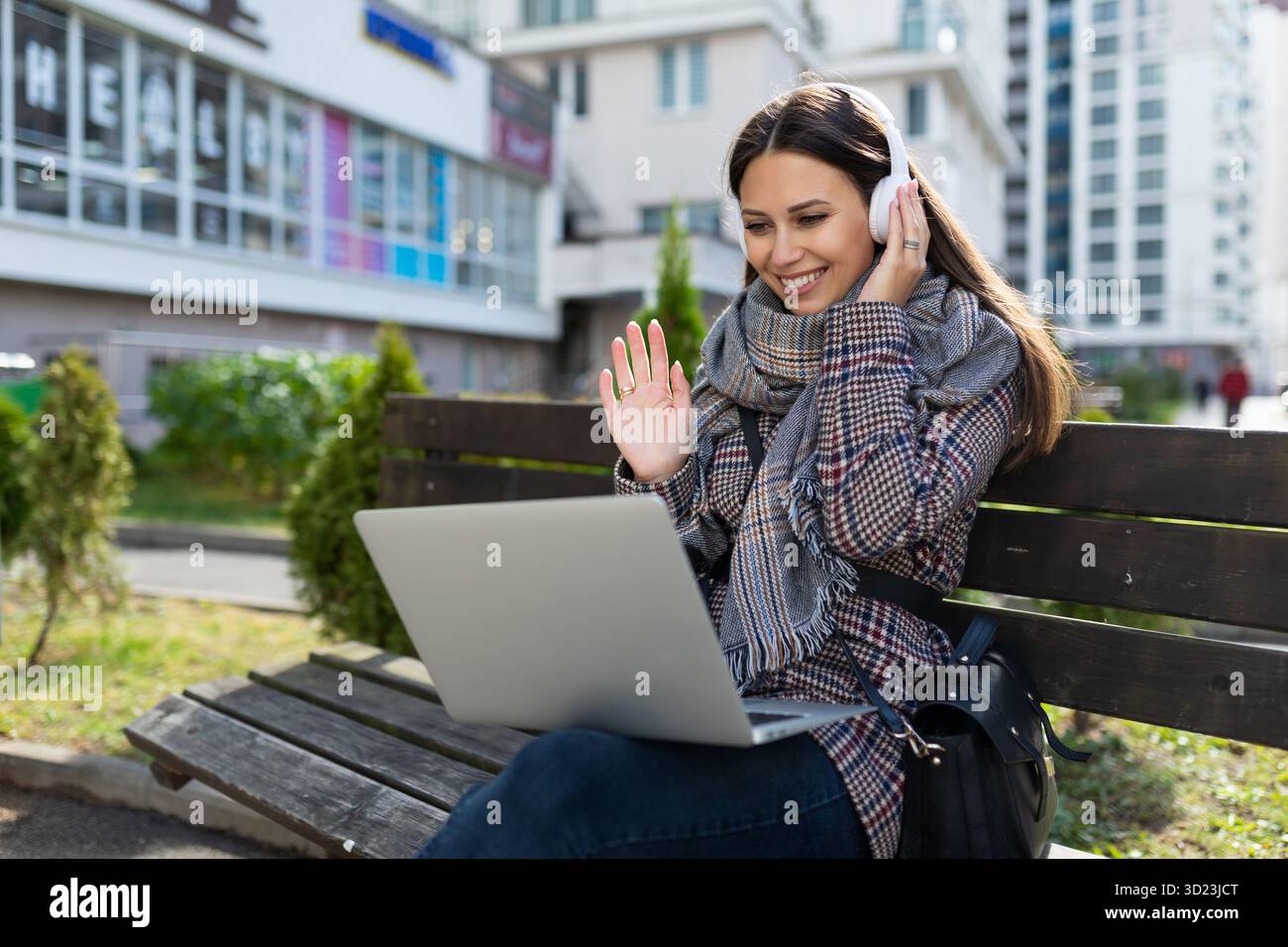 Giovane donna con un notebook in ginocchio in cuffia all'esterno sorridente con piacere e con le mani in alto Foto Stock