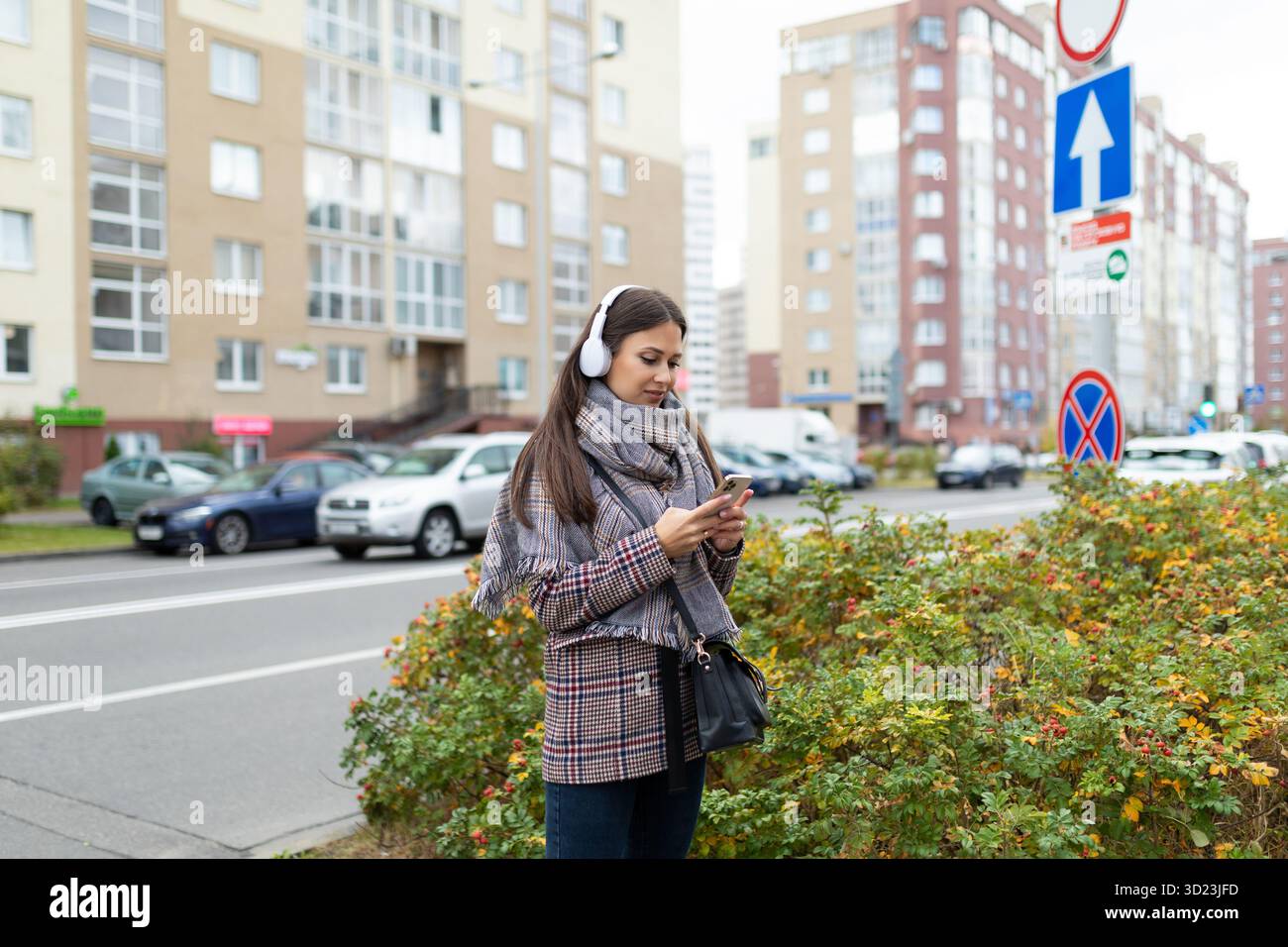 Una giovane donna elegante in giro con le cuffie guarda un telefono cellulare Foto Stock