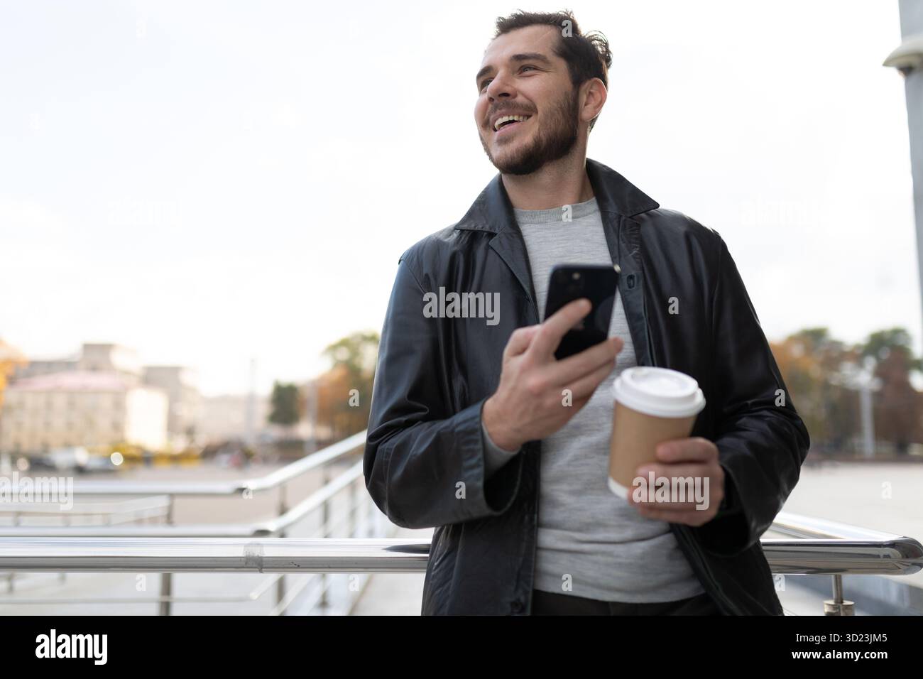 Un uomo con un cellulare in città che beve caffè Foto Stock