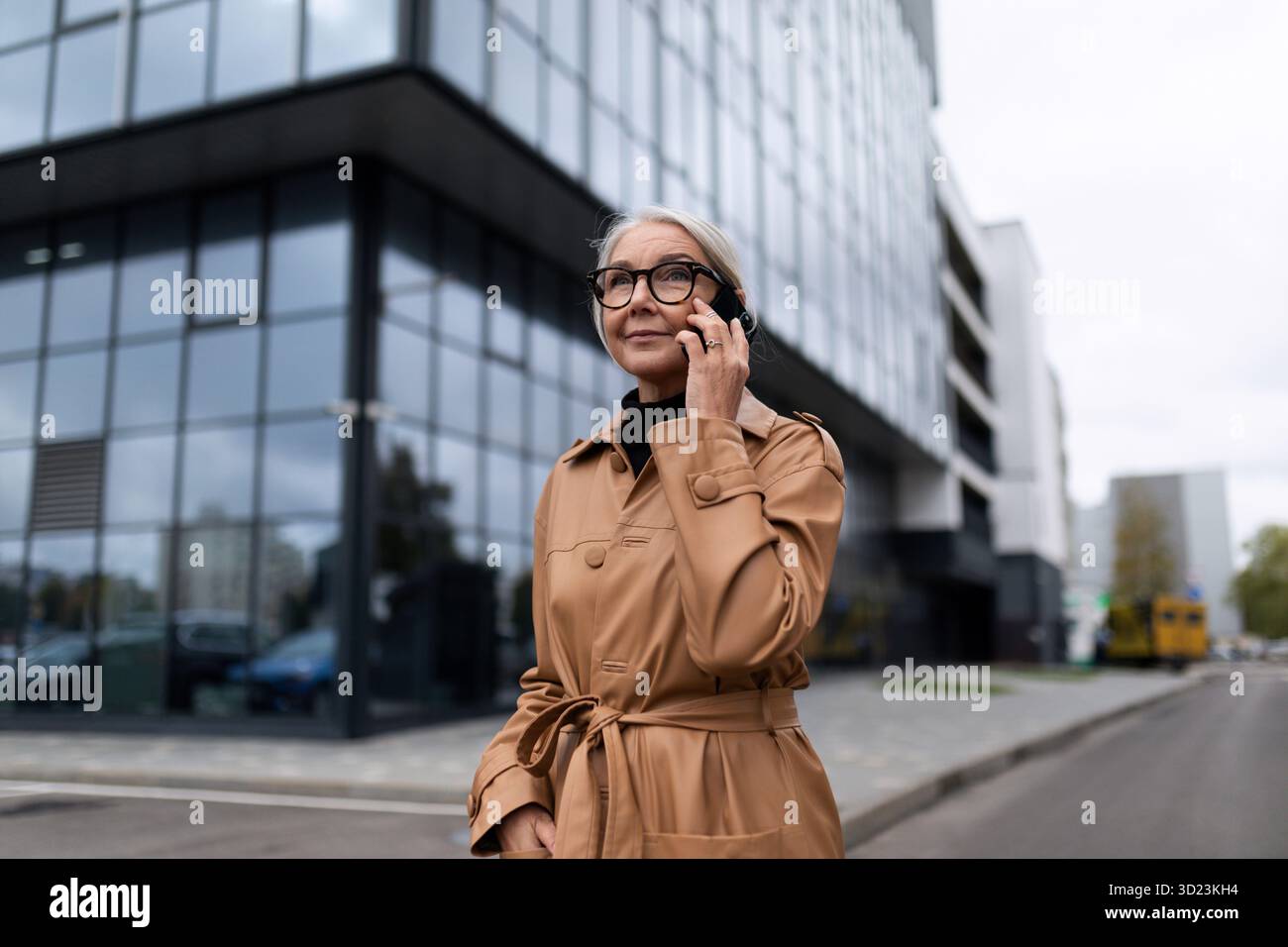 Donna caucasica di alto livello che parla al telefono sullo sfondo di un edificio di uffici Foto Stock