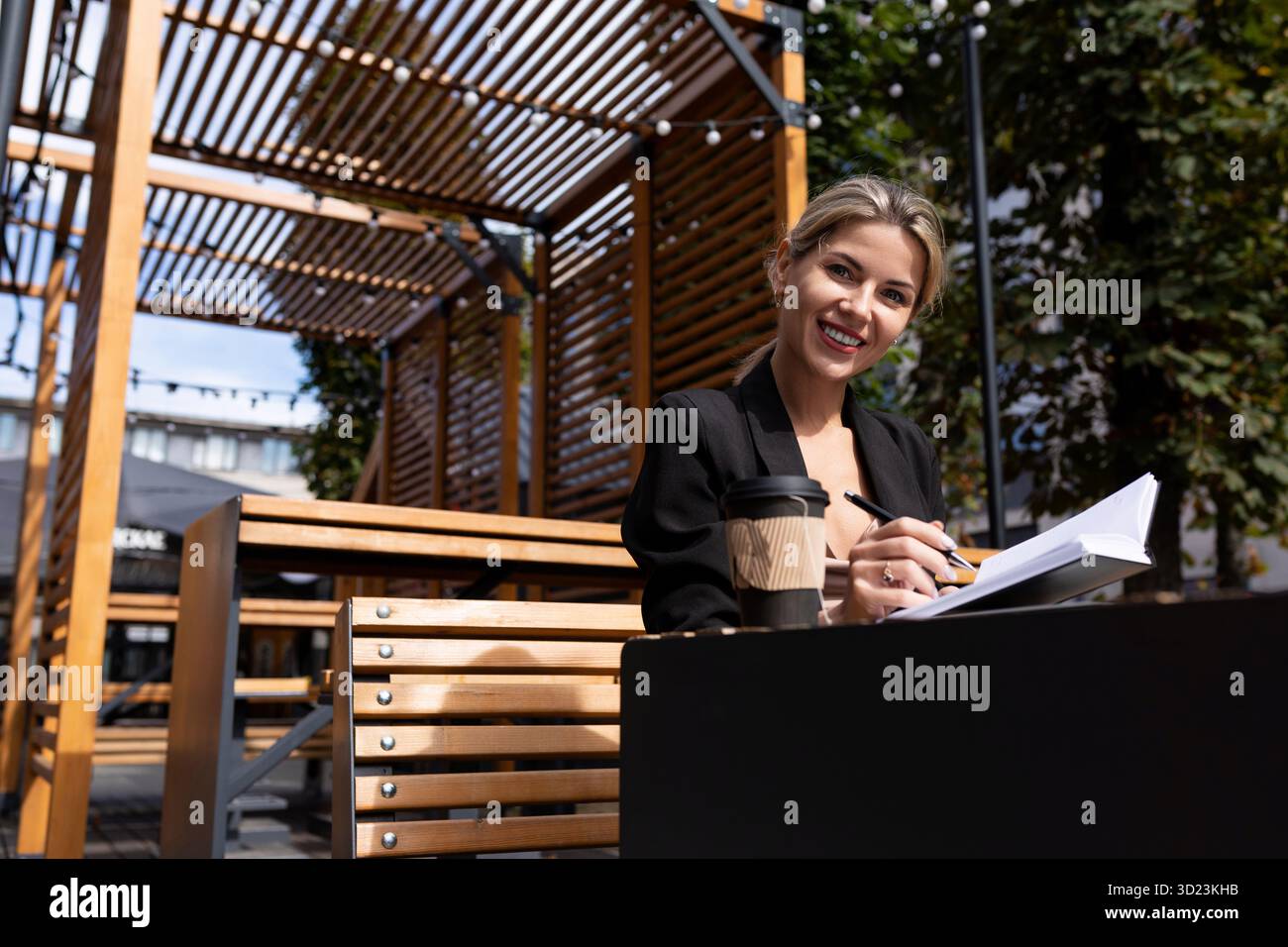 Donna d'affari di successo che lavora all'aperto bevendo caffè e prendendo appunti nel suo diario Foto Stock