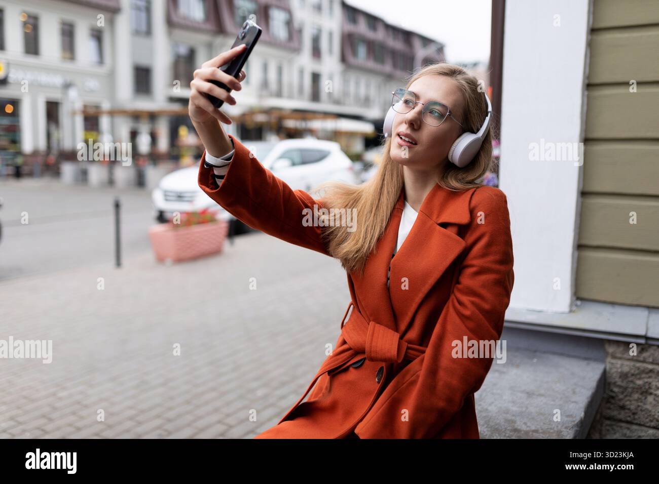 La giovane donna caucasica con le cuffie fa selfie in città Foto Stock