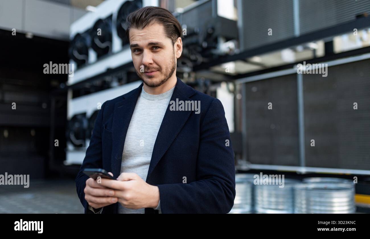 Ingegnere di impianti di refrigerazione industriale con una faccia seria che regge un telefono cellulare, concetto di manutenzione professionale o Foto Stock