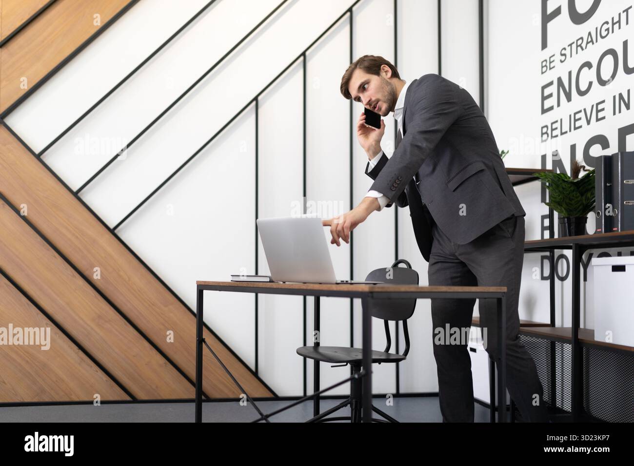 Uomo d'affari di successo che parla al telefono al desktop con un portatile in ufficio Foto Stock