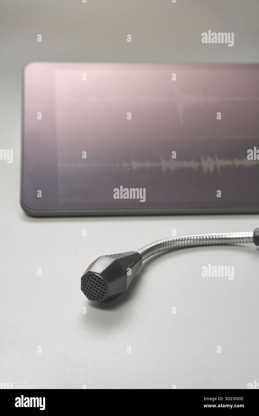 Microfono con tablet che visualizza le forme d'onda audio su una superficie grigia Foto Stock