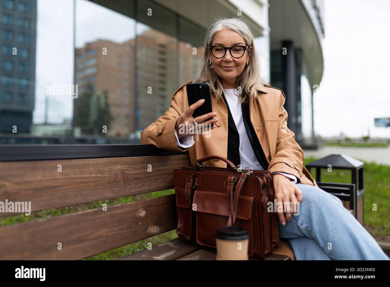 Una donna anziana con un telefono cellulare si siede su una panchina all'esterno Foto Stock