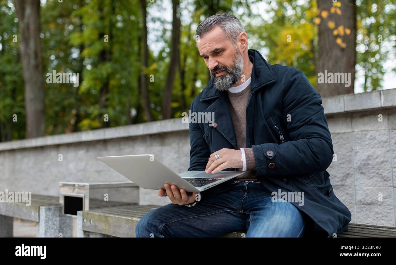 Uomo d'affari che lavora online con un laptop nel parco cittadino Foto Stock