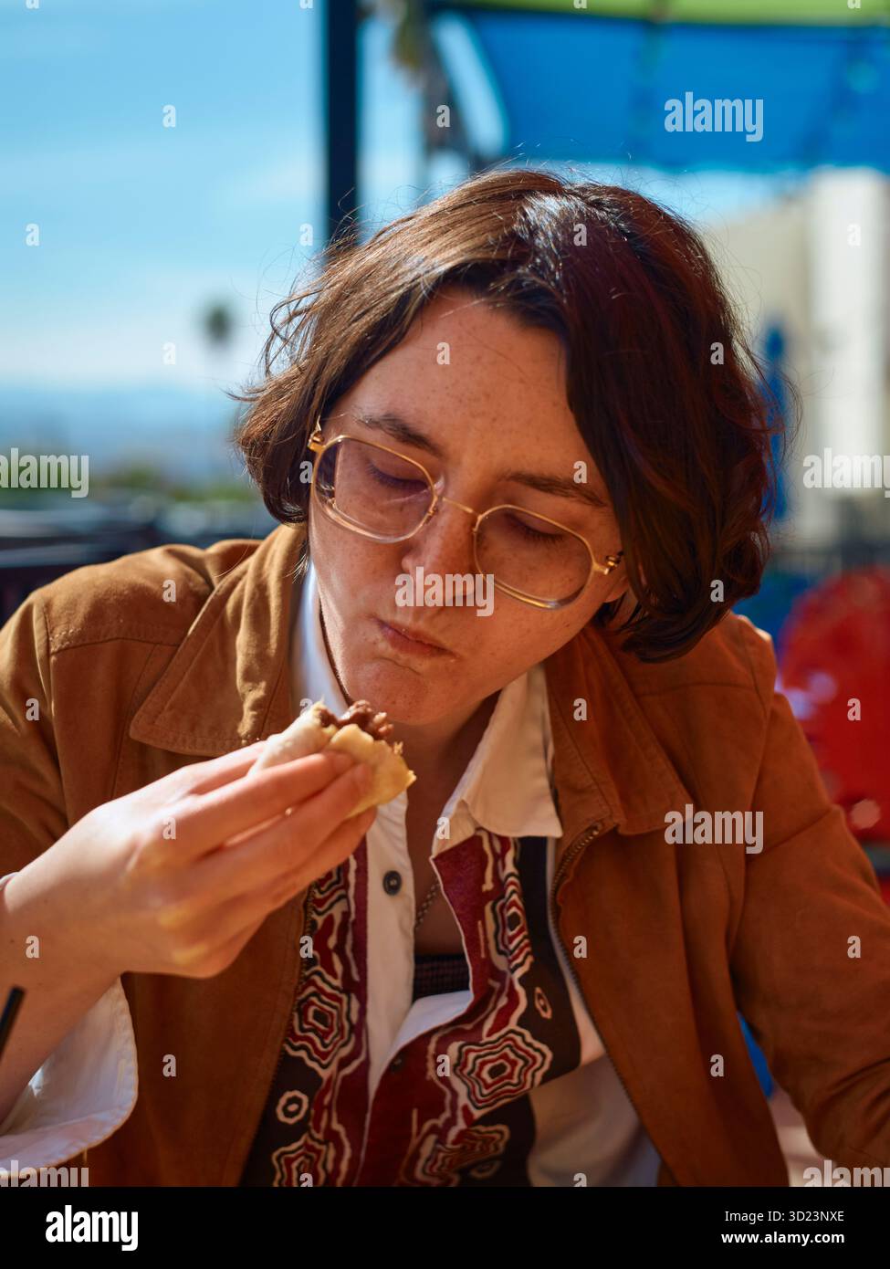 Giovane donna che mangia all'aperto in un bar dai colori vivaci in una giornata di sole. California, Stati Uniti Foto Stock