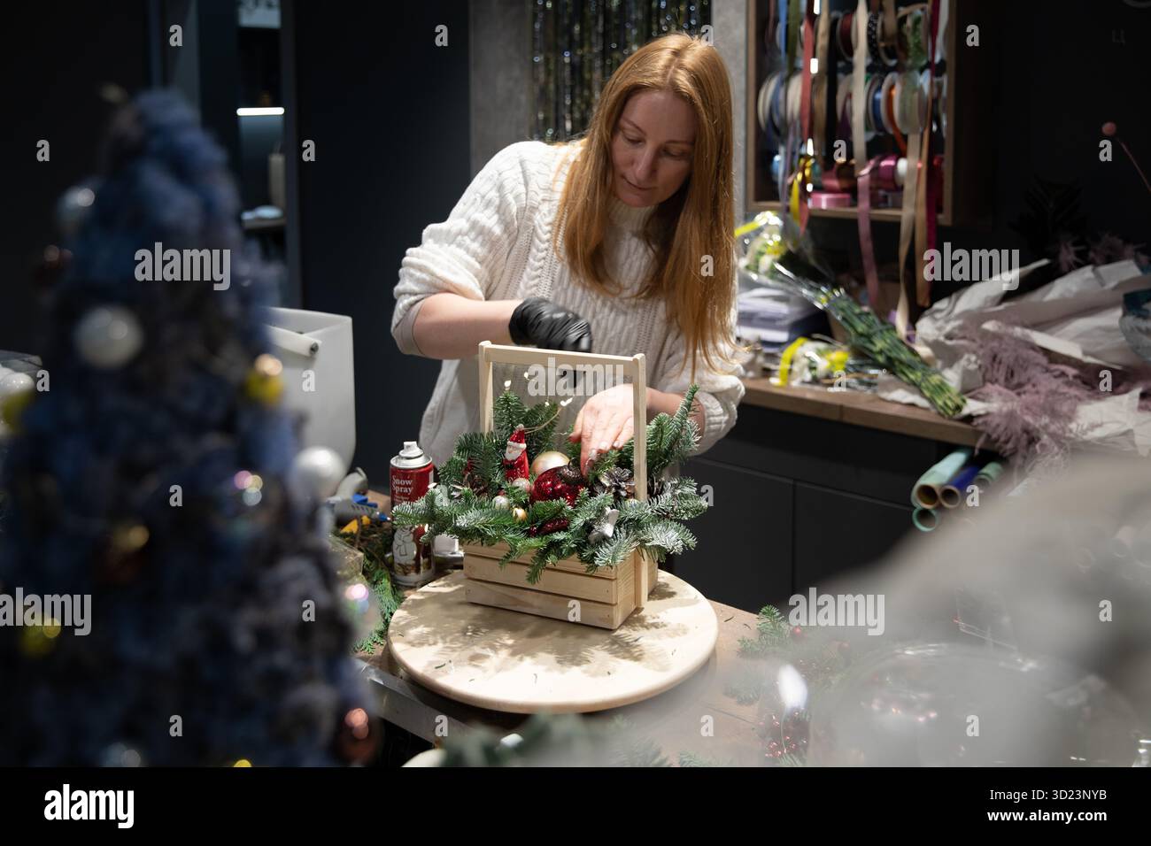 Minsk, Bielorussia - 20 dicembre 2021: Un lavoratore negozio di fiori crea una composizione floreale in una scatola di legno a tema natalizio Foto Stock