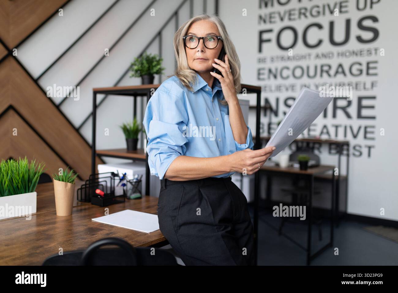 Una donna d'affari di cinquant'anni con documenti in mano parla su un cellulare in un ufficio moderno. Financial Business Analyti Foto Stock