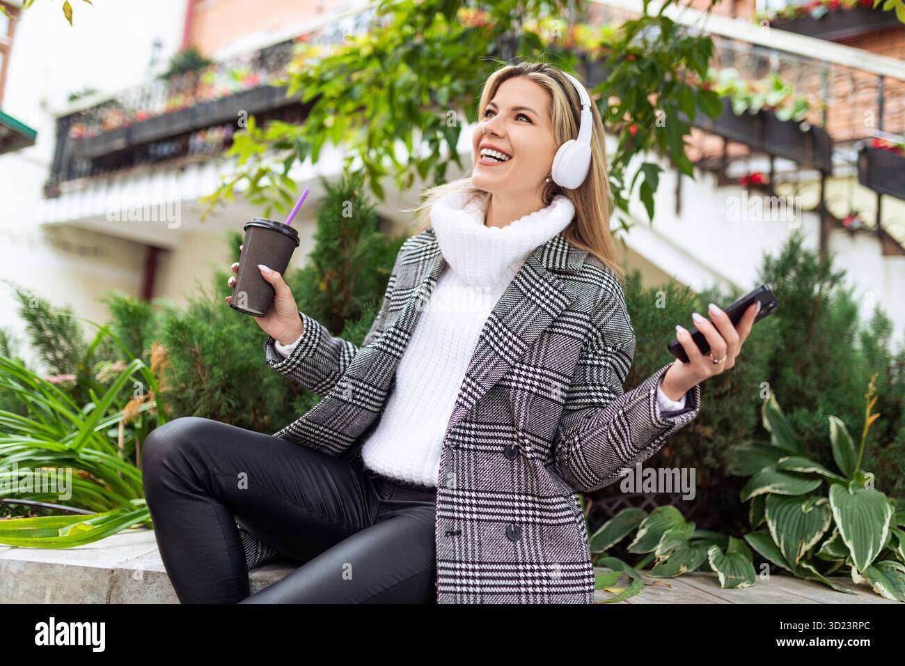 Una donna adulta ama ascoltare musica con le cuffie sullo sfondo di un parco cittadino Foto Stock