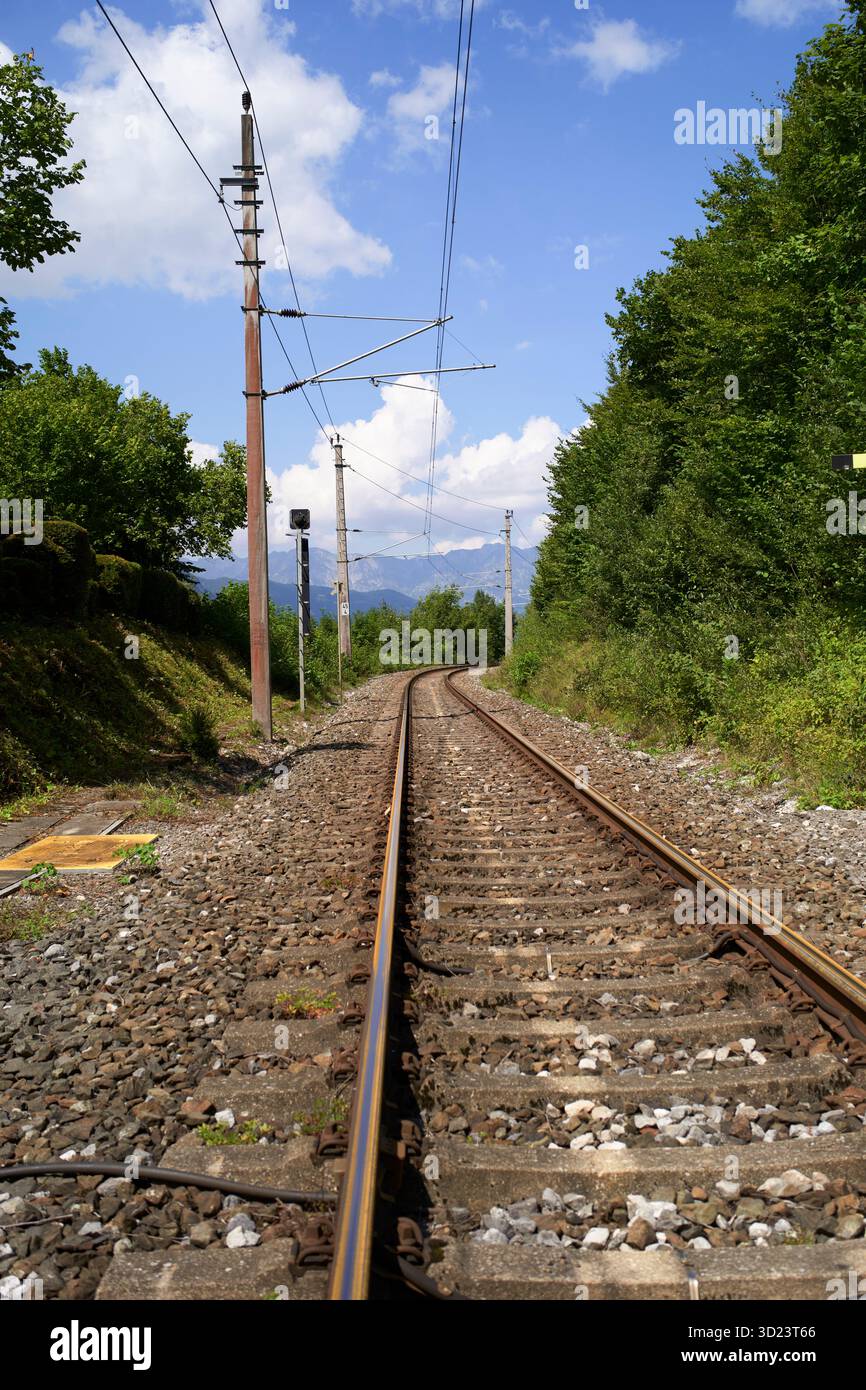 I binari ferroviari si snodano attraverso un lussureggiante paesaggio verde sotto un cielo blu luminoso con nuvole. Salzkammergut, Monti Dachstein, Austria Foto Stock