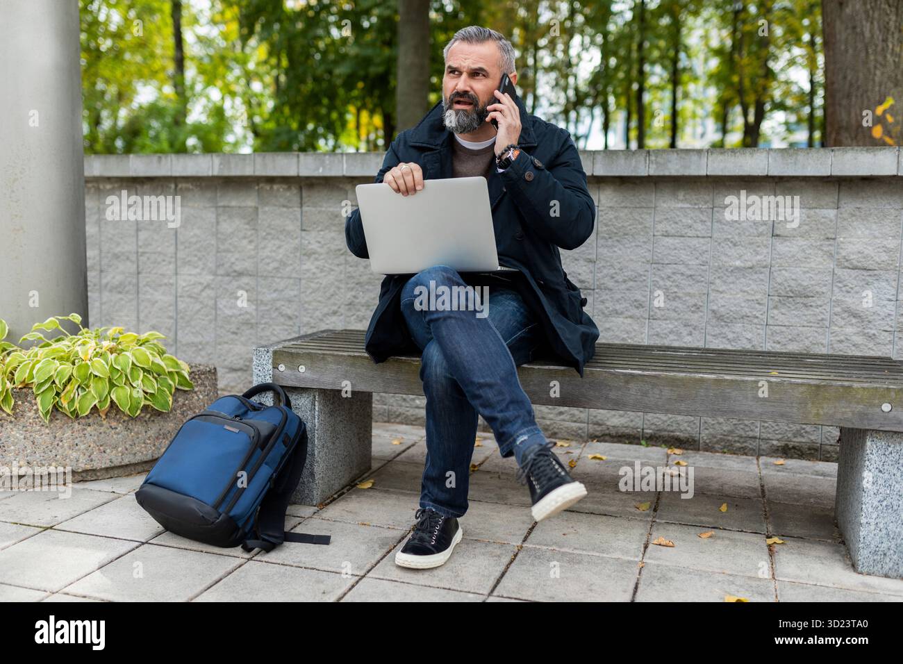 Un uomo maturo che lavora al portatile fuori che parla al telefono Foto Stock