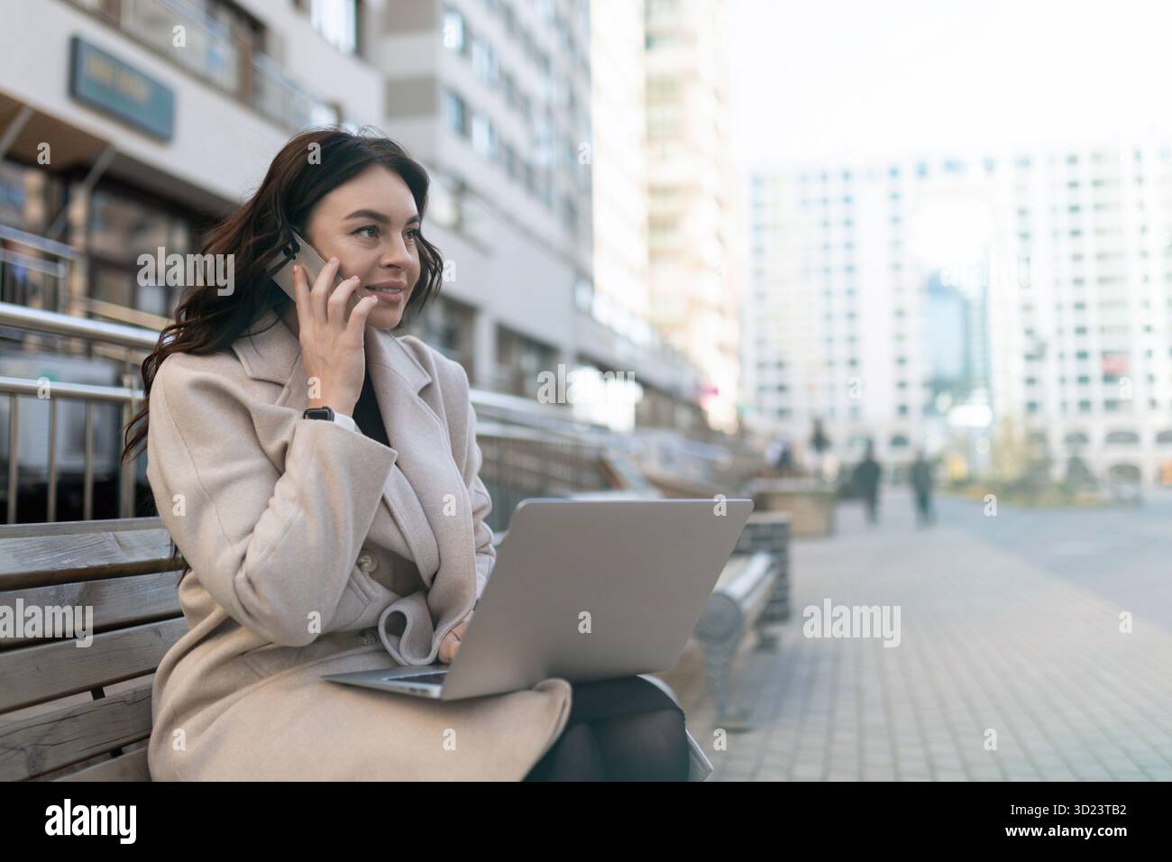 Giovane donna d'affari che parla al telefono cellulare e lavora al computer portatile online fuori dall'ufficio Foto Stock
