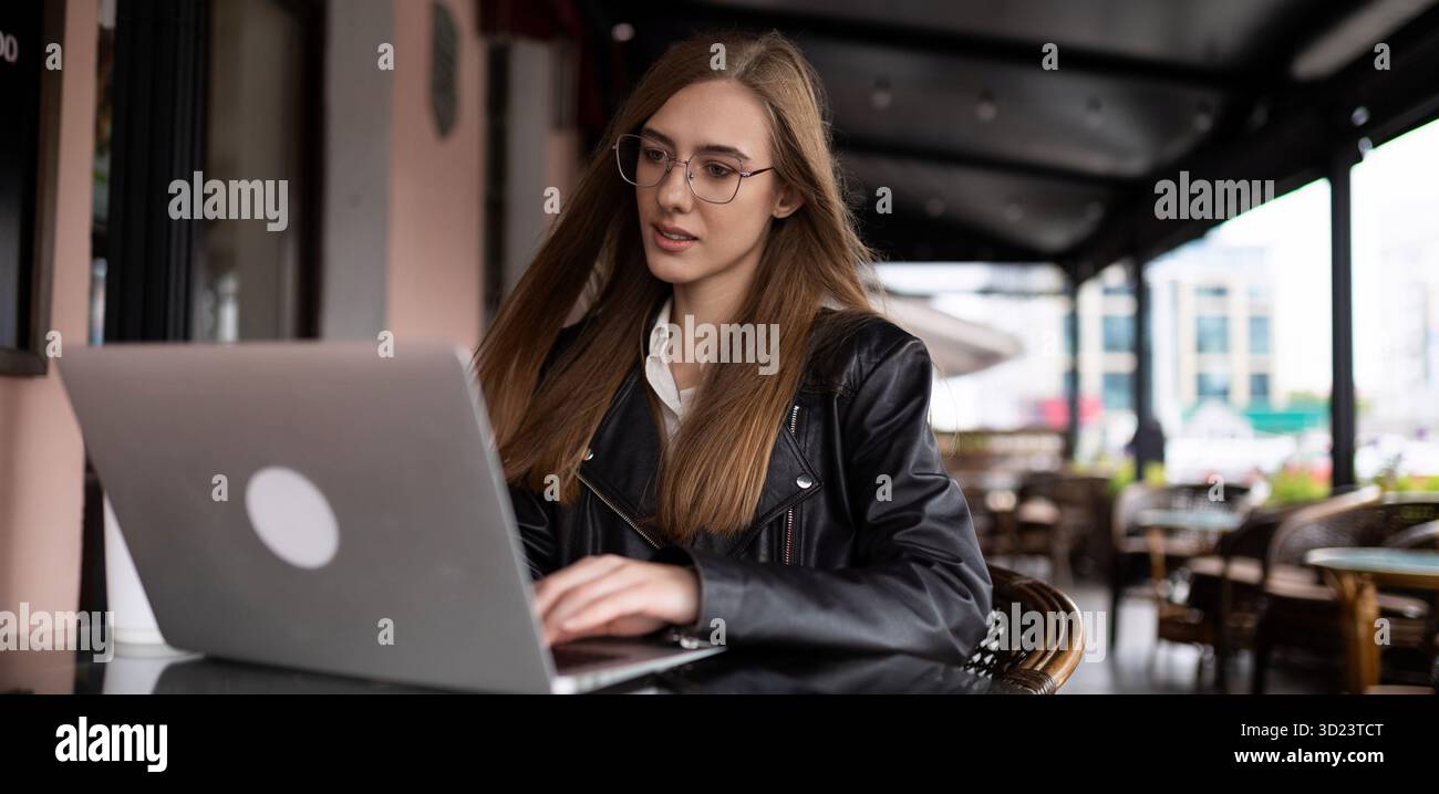 Donna freelance che lavora online con un laptop in un caffè cittadino Foto Stock