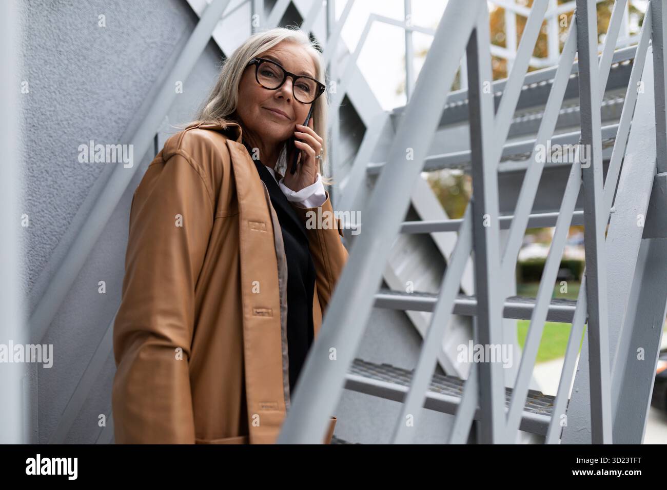 Donna d'affari matura che parla al telefono sulle scale fuori Foto Stock