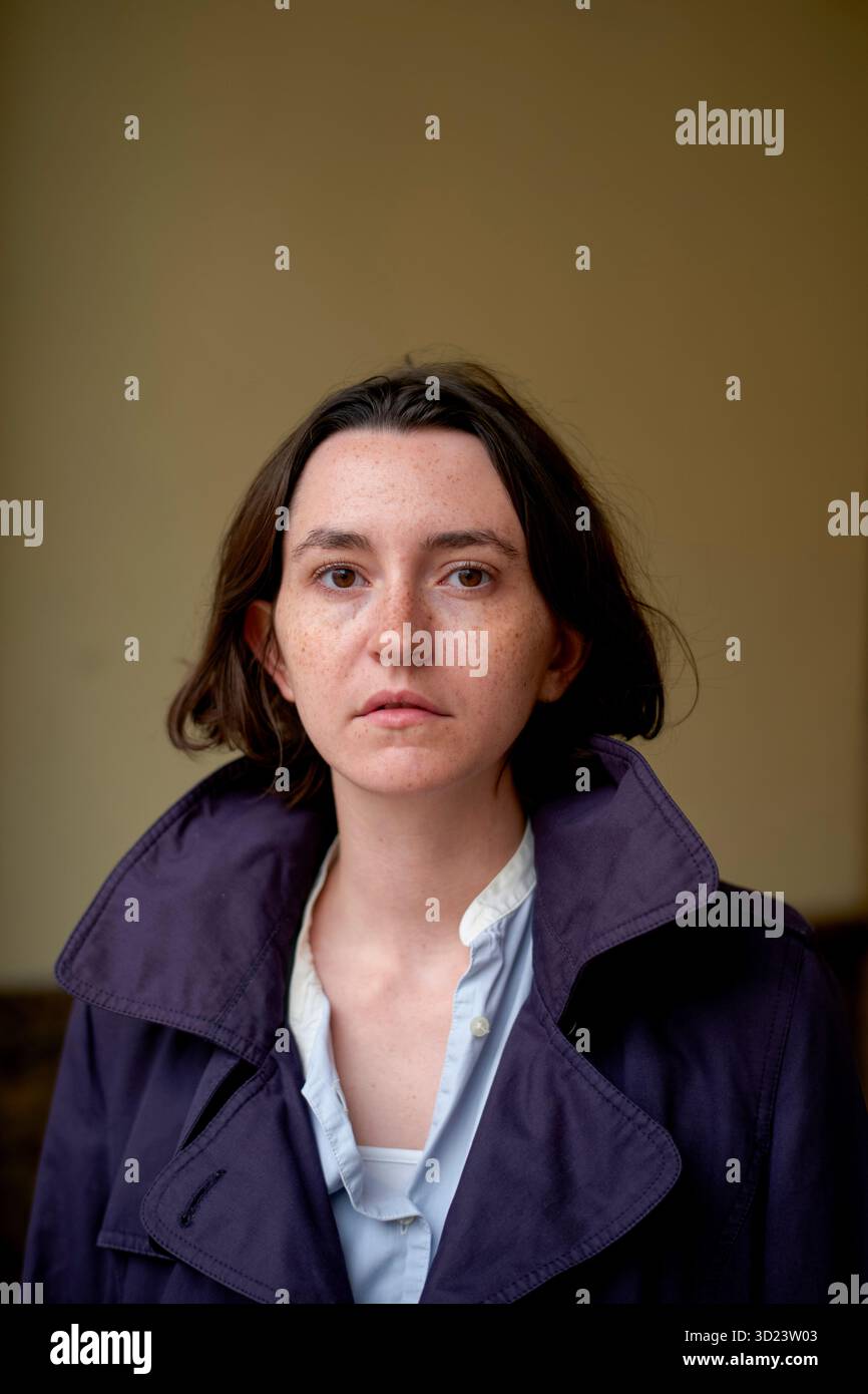 Una donna con i capelli corti marroni che indossa un cappotto viola e una camicia bianca fissa la fotocamera. Bruxelles, Belgio Foto Stock