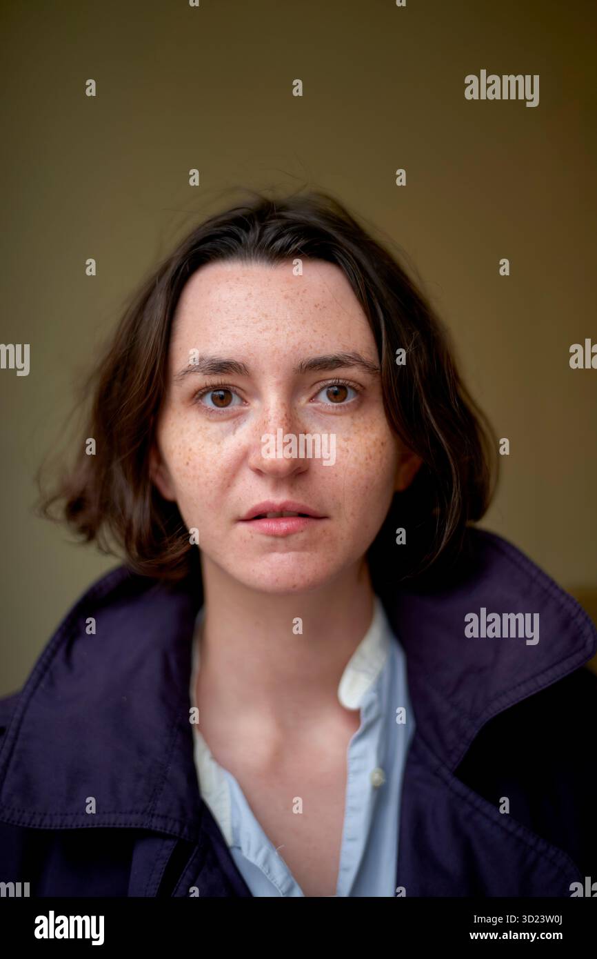 Donna con un cappotto scuro e una camicia blu che guarda direttamente la fotocamera in interni. Bruxelles, Belgio Foto Stock