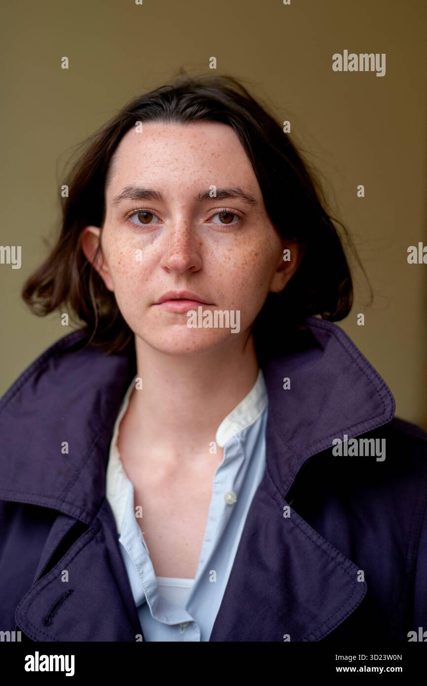 Una donna con i capelli corti marroni che indossa un cappotto viola e una camicia bianca fissa la fotocamera. Bruxelles, Belgio Foto Stock