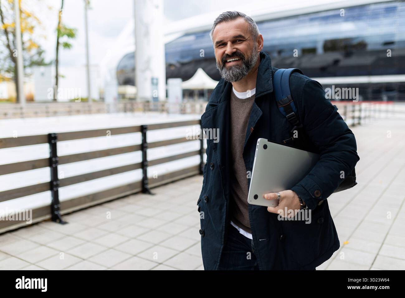 Uomo maturo con laptop e zaino che si affrettano a lavorare sorridendo guardando la fotocamera Foto Stock