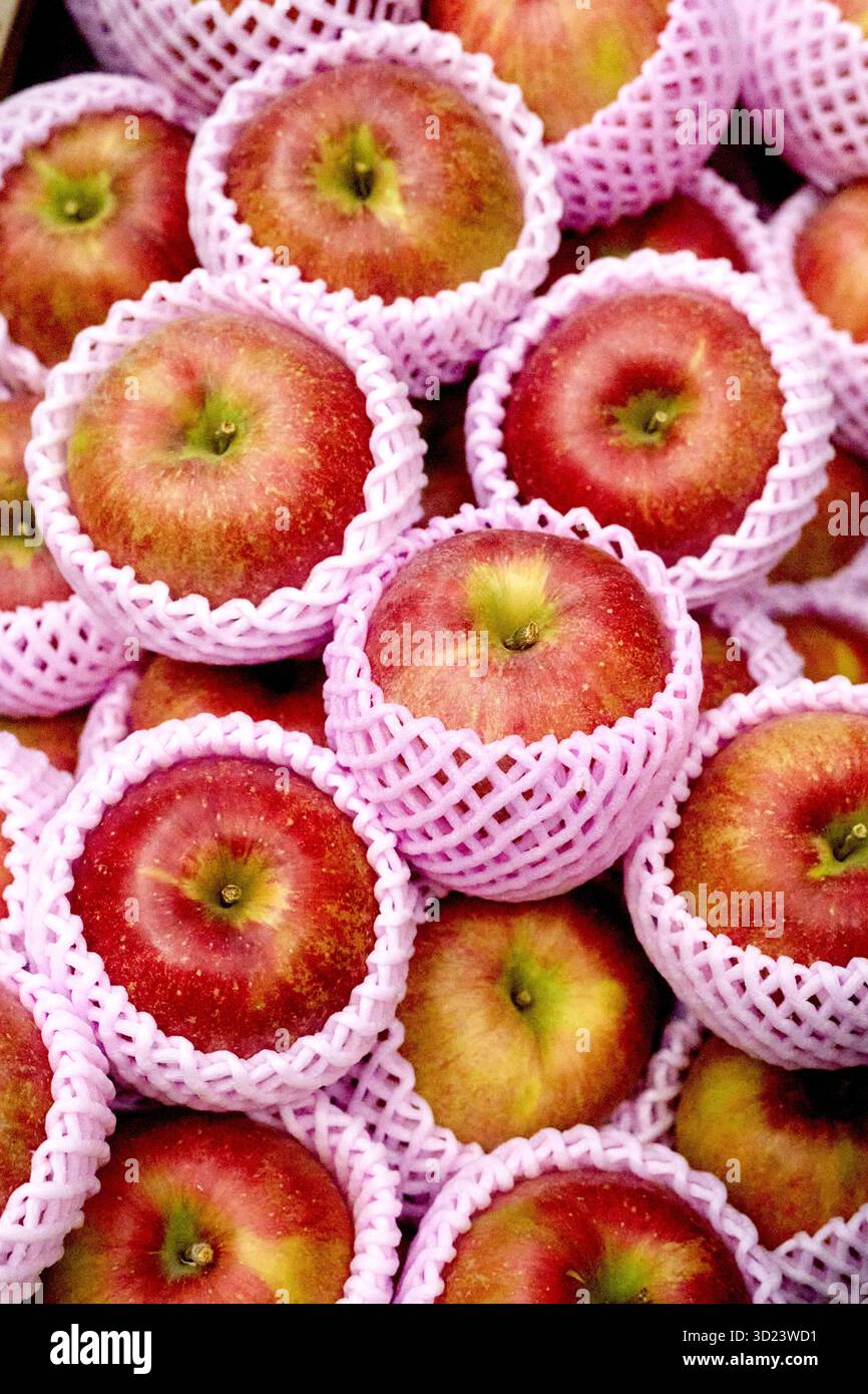 Mele rosse avvolte in rete protettiva, disposte in un mucchio in una bancarella del mercato. Foto Stock