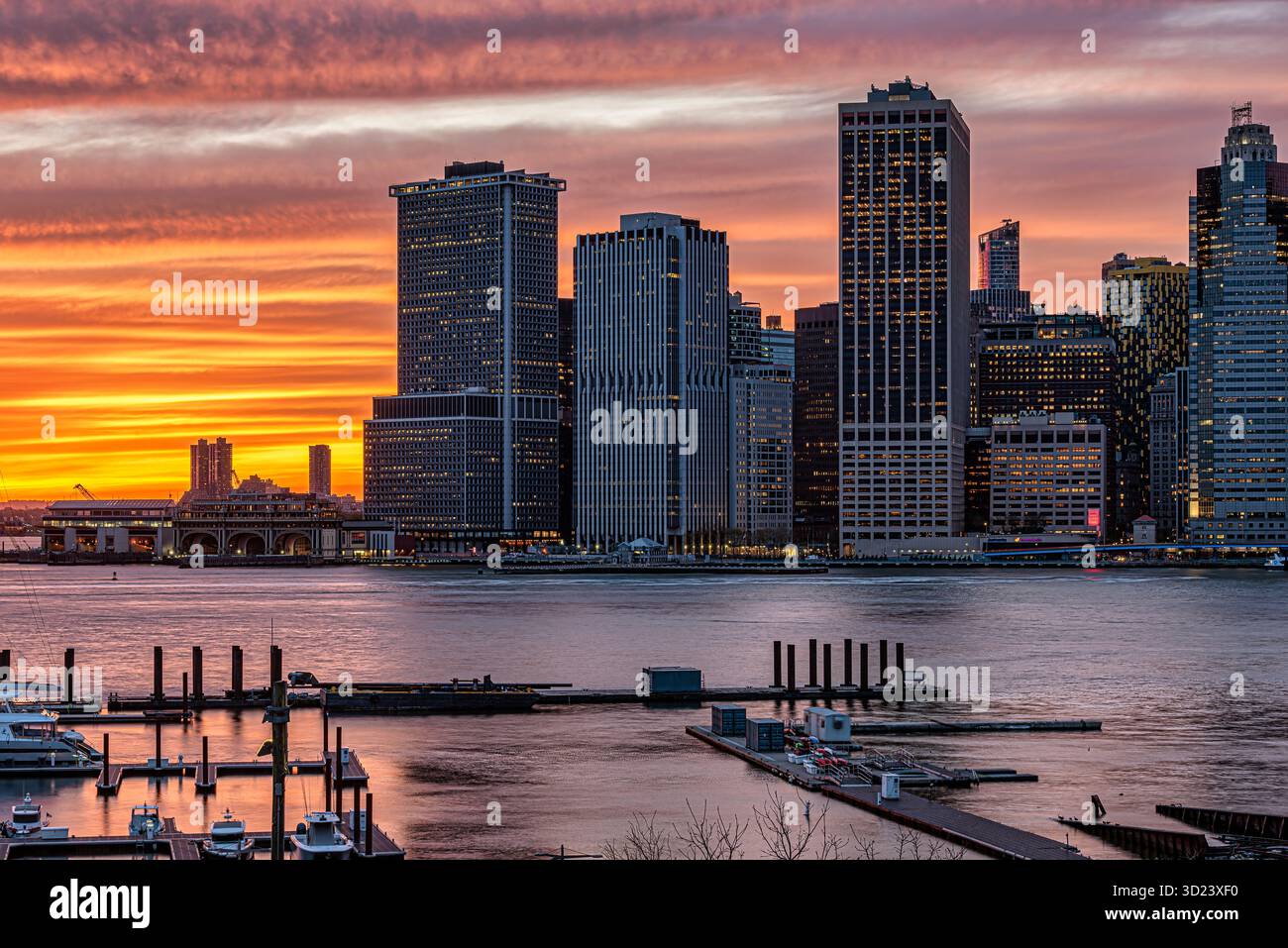 Tramonto vibrante sullo skyline della città con edifici alti e un fiume calmo in primo piano. New York, New York, Stati Uniti Foto Stock