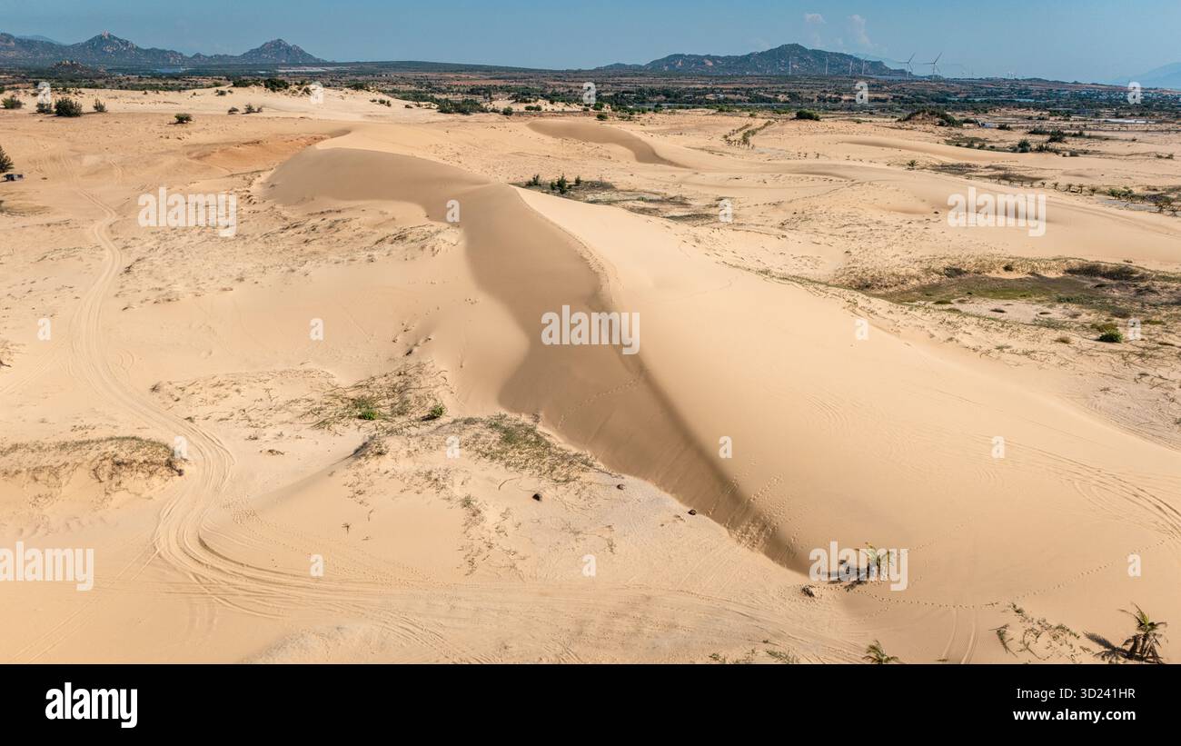 Veduta aerea delle dune di sabbia di Phan Rang, Vietnam: Ampio paesaggio desertico con dune scolpite e montagne lontane sotto il cielo blu. Foto Stock