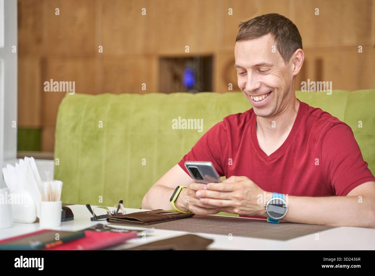 Adulto caucasico sorridente che utilizza lo smartphone in un ambiente informale e moderno Foto Stock