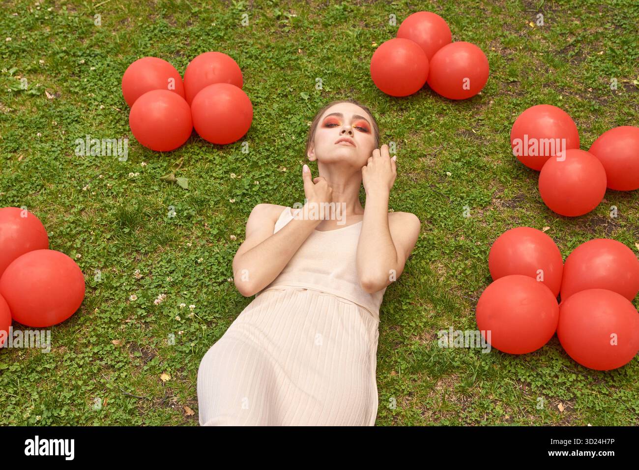 Giovane donna caucasica che si rilassa sull'erba circondata da palloncini rossi all'aperto Foto Stock