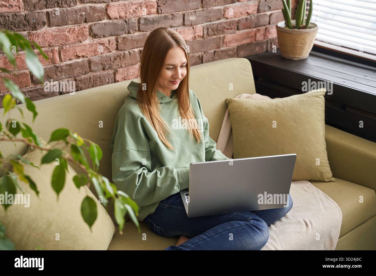Giovane donna caucasica che lavora su un laptop in un ambiente accogliente con mattoni Foto Stock