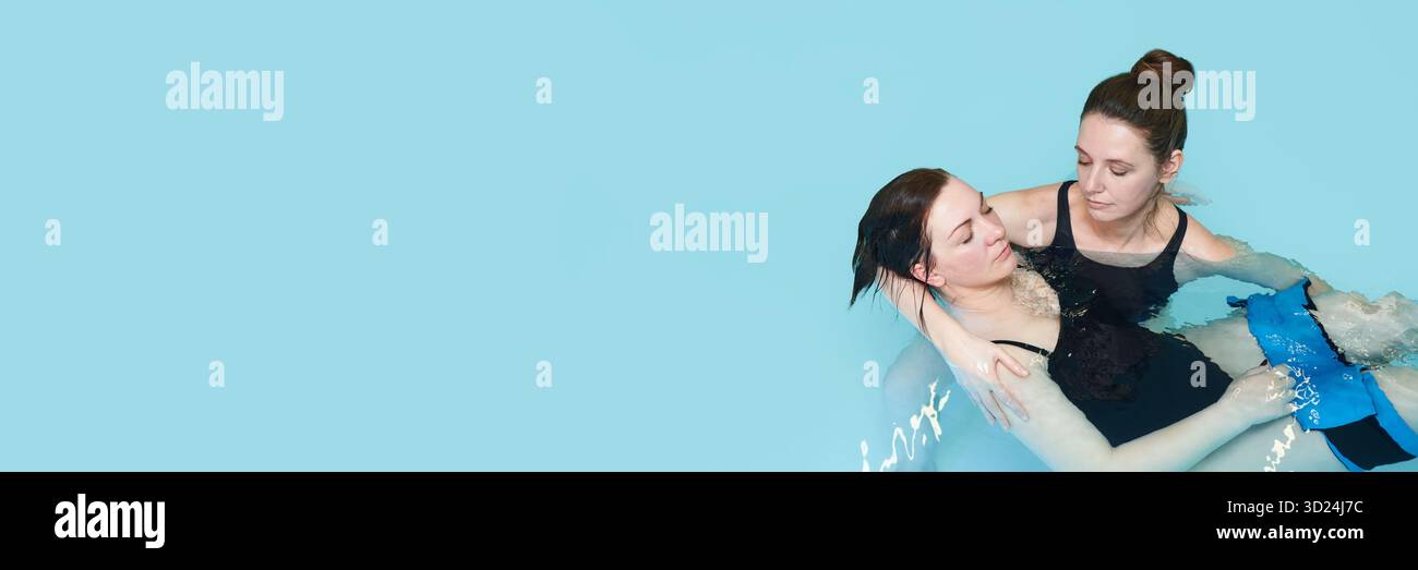 Due donne caucasiche che praticano tecniche di terapia dell'acqua in un ambiente piscina Foto Stock