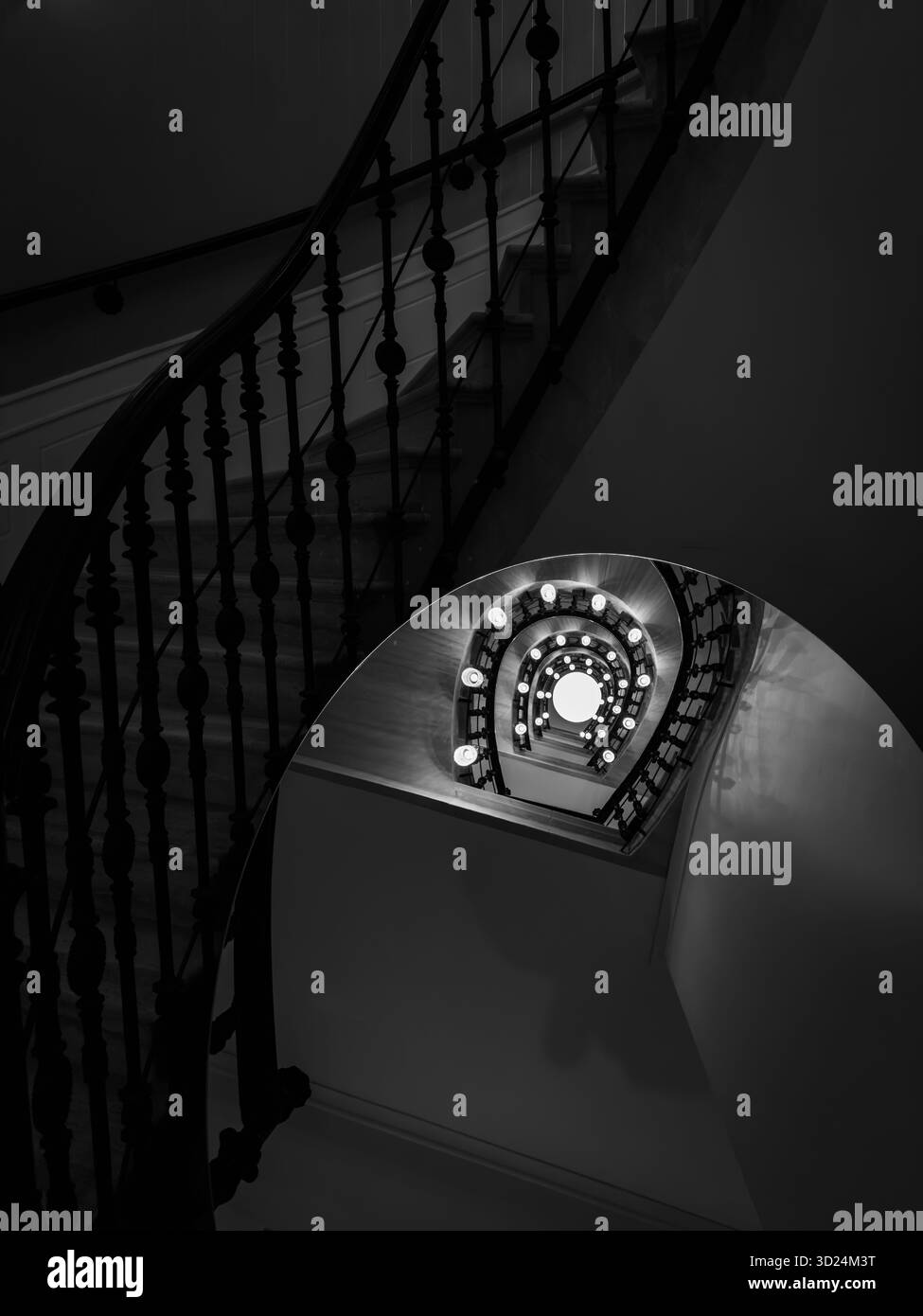Scala a spirale monocromatica con luci circolari illuminate lungo la ringhiera crea profondità e mistero Foto Stock