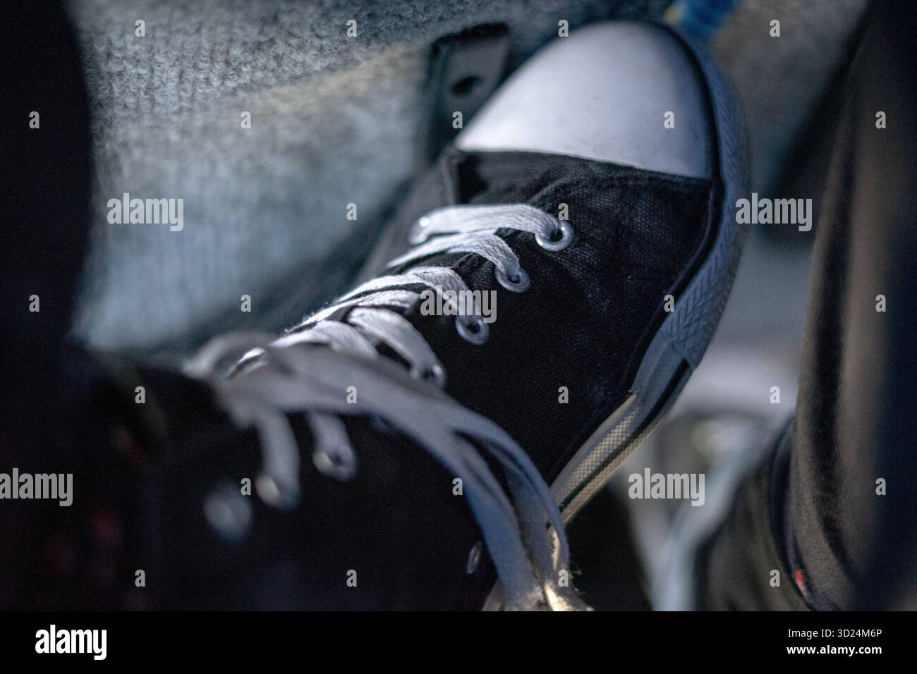 Primo piano di una sneaker in tela bianca e nera con lacci, scattata in condizioni di scarsa illuminazione. Foto Stock