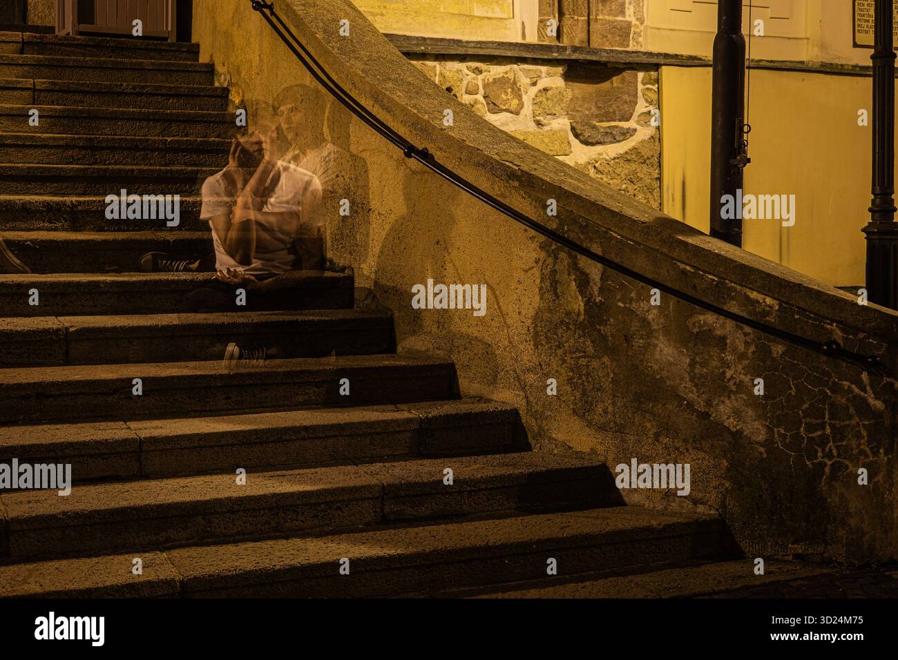 Personaggio spettrale a lunga esposizione seduto su antiche scale di pietra di notte in una città storica. Foto Stock